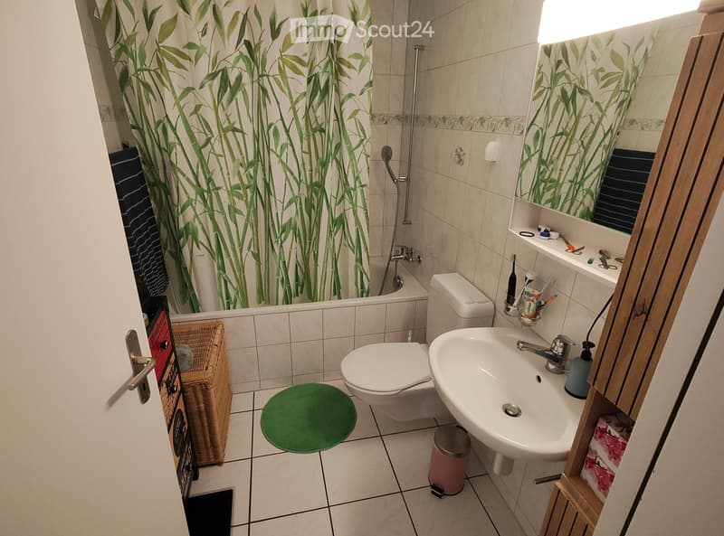 Bathroom with a toilet, sink, mirror, bathtub with a bamboo-patterned shower curtain, and various toiletries on the sink counter.