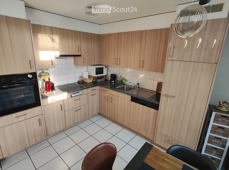 Modern kitchen with light wood cabinets, granite countertops, and stainless steel appliances. Includes an oven, microwave, coffee maker, sink, and a small dining area with a table and chairs.