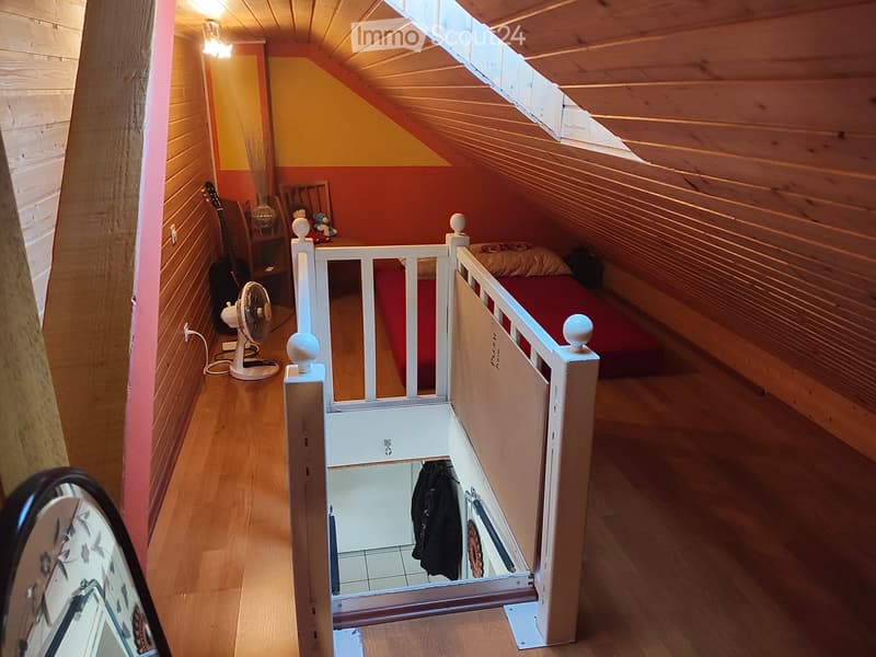 Cozy attic bedroom with wooden walls and slanted ceiling, featuring a bed, guitar, fan, and a small wardrobe.