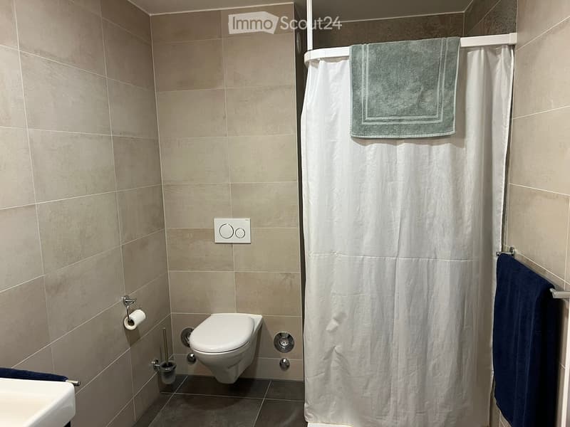 Modern bathroom with beige tiled walls, a toilet, a shower curtain, and towels.