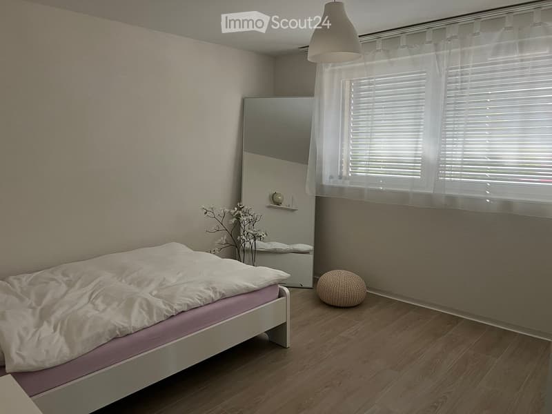 Modern bedroom with a white bed, pink mattress, large mirror, spherical chair, and a small flower arrangement near the window.