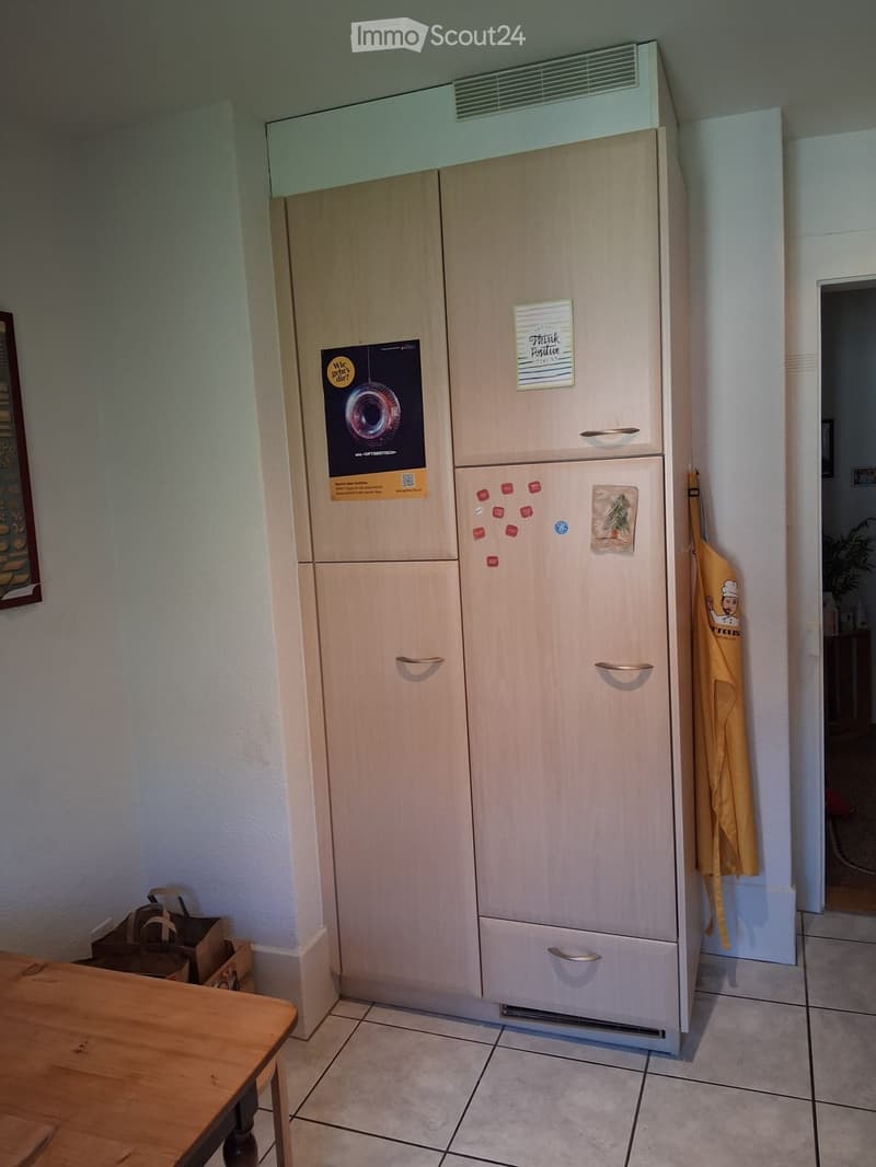 A modern kitchen with a large refrigerator, a wooden table, and an oven mitt hanging on the wall.
