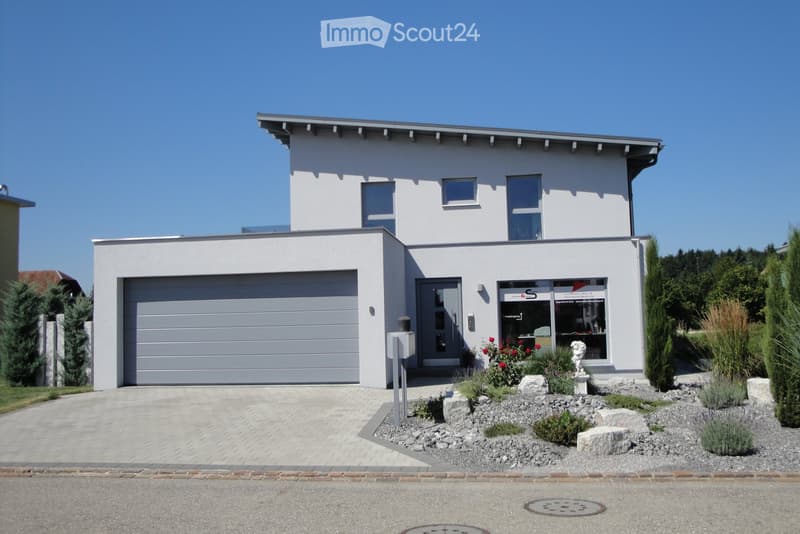 Modern two-story house with white exterior, grey garage door, and landscaped front yard with decorative rocks and plants.
