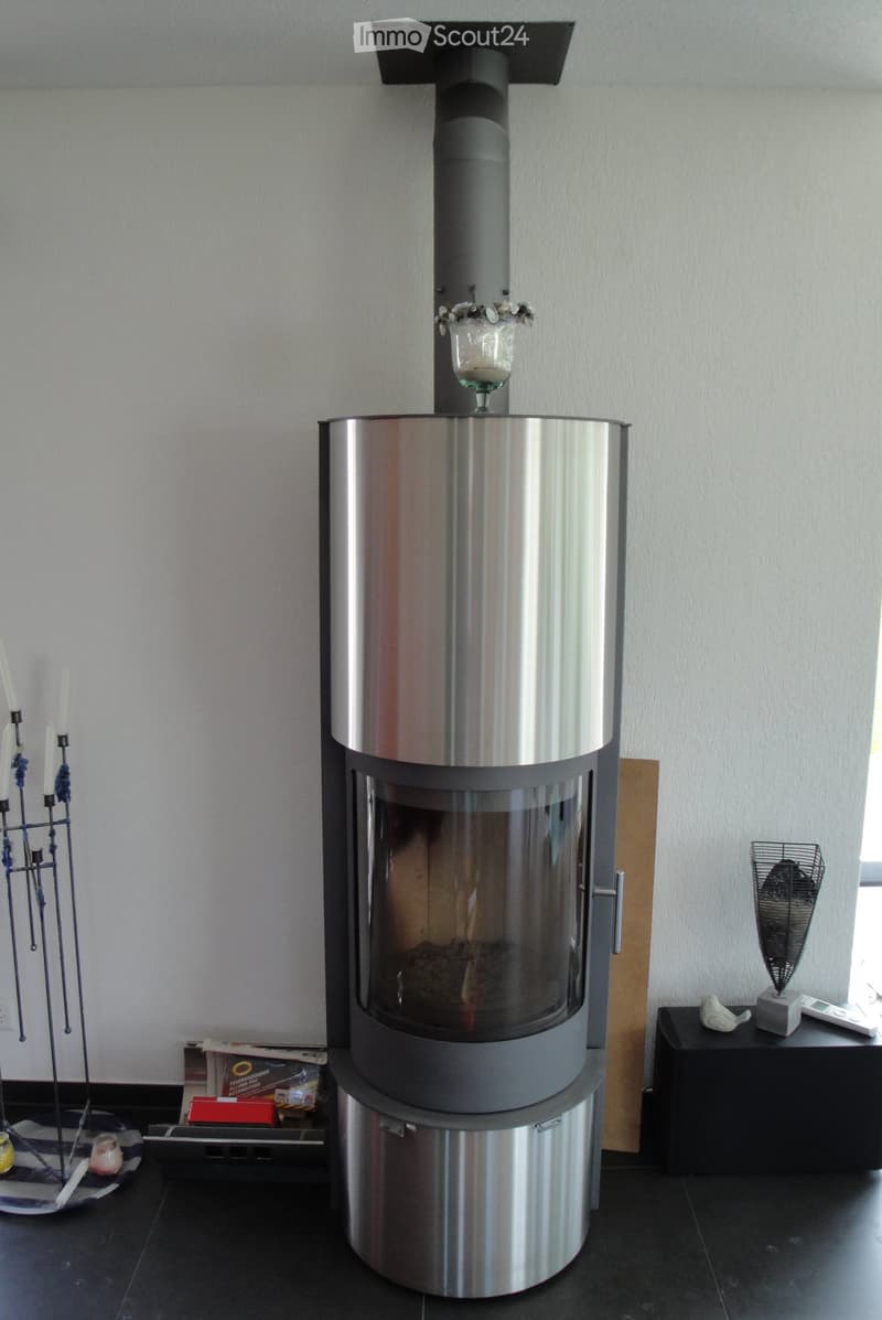 Modern living room with a sleek, stainless steel fireplace as the focal point, accompanied by a candle holder, small table, decorative fan, and remote control on a side table.