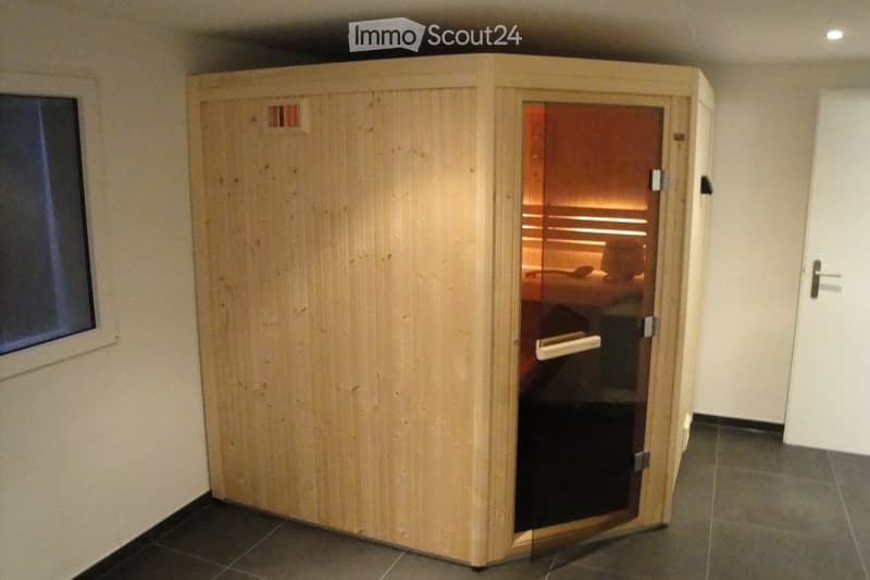 A wooden sauna unit with a glass door is placed in a room with tiled flooring and white walls.