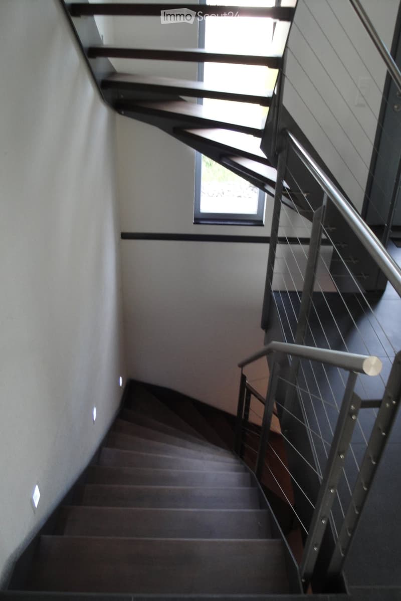 Modern staircase with wooden steps, metal railing, and built-in lighting, leading upwards with a window at the top.