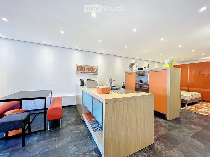 Modern kitchen with a central island, sink, and orange cabinets. Includes a small seating area with a table and chairs.