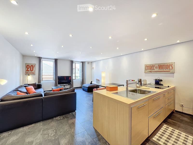 Open-plan living and kitchen area with a sectional sofa, coffee table, kitchen island, sink, and various appliances.