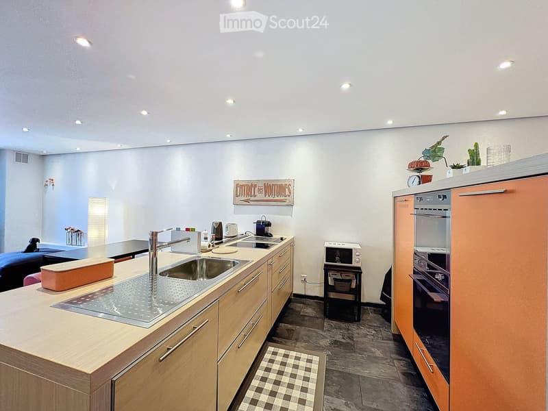 Modern kitchen with wooden cabinets, stainless steel sink, oven, microwave, coffee maker, and a small seating area with a table and chairs.
