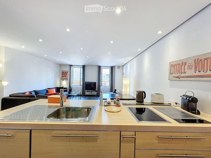 Modern open-plan living and kitchen area with a sofa, coffee table, television, and a kitchen island with a sink, stove, and various appliances.