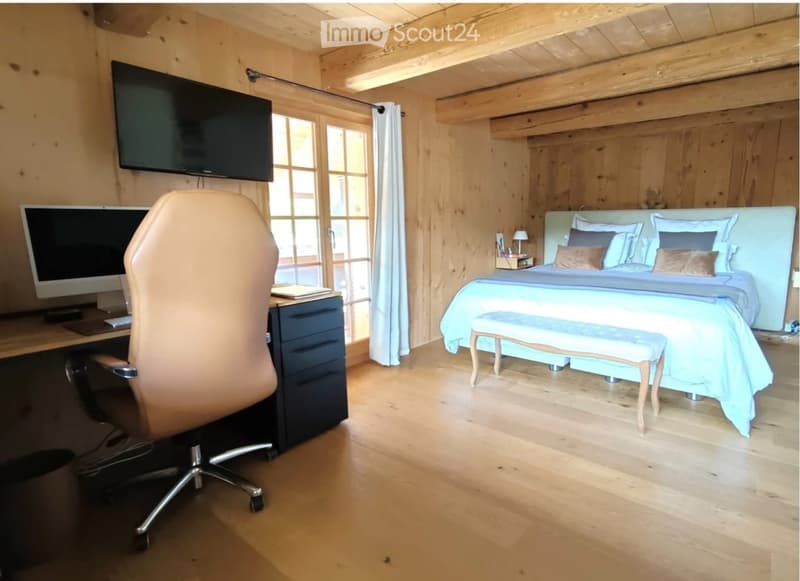 Cozy wooden bedroom with a large bed, a chair, a stool, a screen, a table, and a lamp.