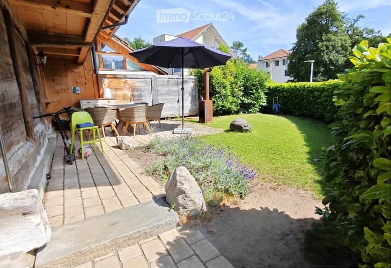 Garden with a patio area, outdoor dining set, umbrella, bicycle, and surrounding greenery.