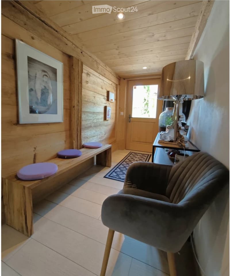 Cozy hallway with wooden walls and ceiling, featuring a bench with purple cushions, a modern chair, a small table with a lamp, and artwork on the wall.