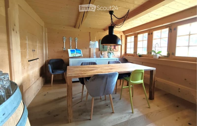 A cozy, wooden-paneled room with a dining table and chairs, a screen, a lamp, and a small cabinet with decorative items.