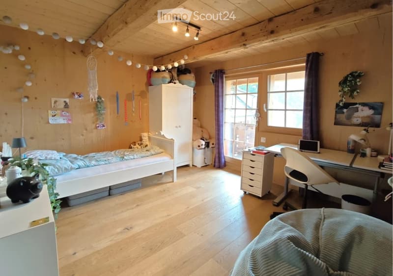 Cozy wooden bedroom with a single bed, desk, chair, wardrobe, and decorative items including a dreamcatcher and a plant.