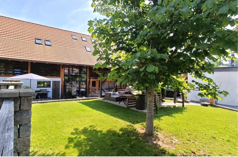 Well-maintained garden with a lush green lawn, a tree, patio furniture, and a modern house with large windows and a wooden deck.