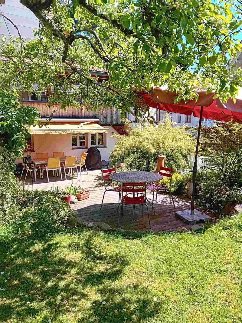 Garden with wooden deck, outdoor dining area, patio furniture, and surrounding greenery.