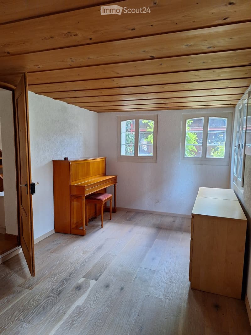 Bright room with wooden ceiling and light wooden flooring, featuring a piano, a matching stool, and a wooden cabinet.