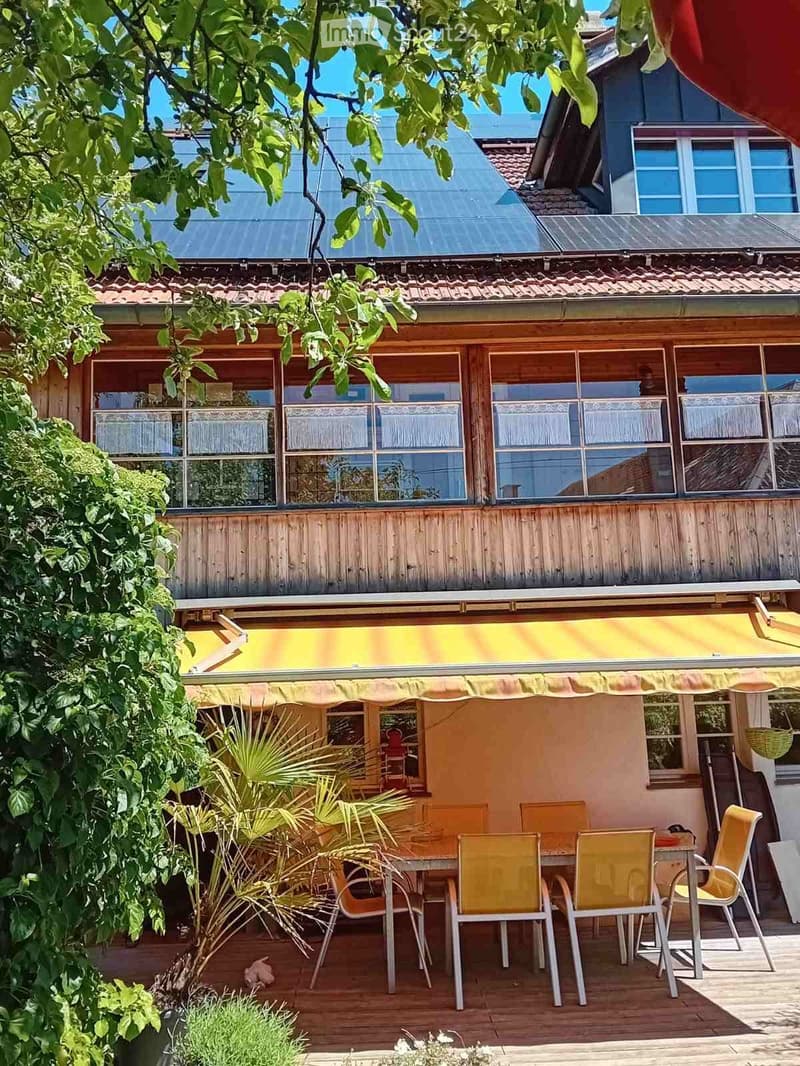 Wooden deck with yellow awning, outdoor dining set, and lush greenery.