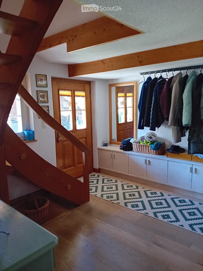 Cozy hallway with wooden floors, exposed wooden beams, built-in storage cabinets, coat rack, and a patterned rug.