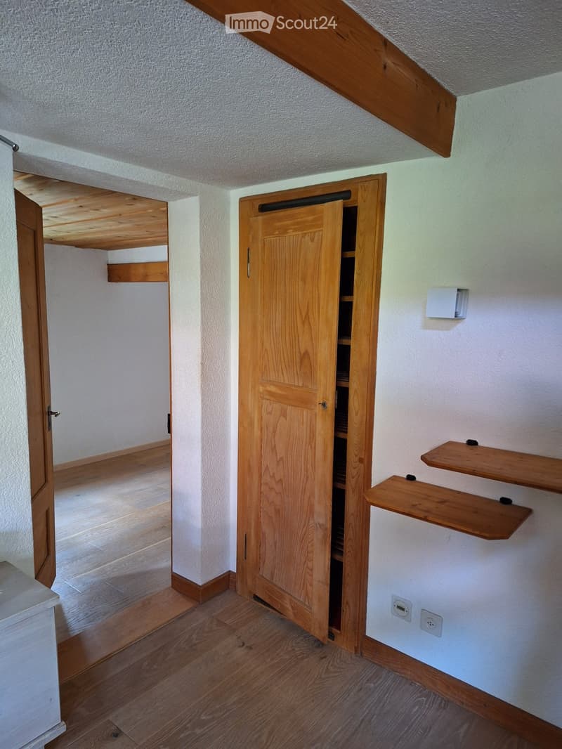 Empty room with wooden floor, white walls, built-in wooden shelves, and an open wooden closet with empty shelves.