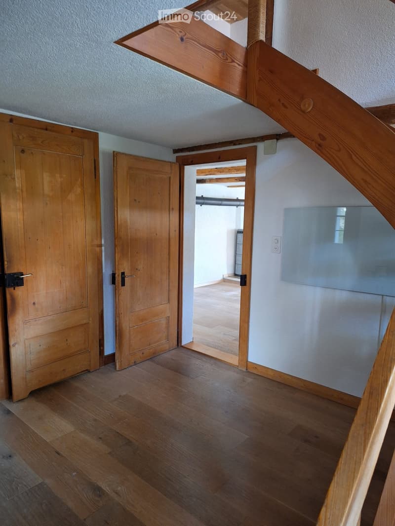 Empty hallway with wooden flooring, light-colored walls, and open wooden doors leading to other rooms.