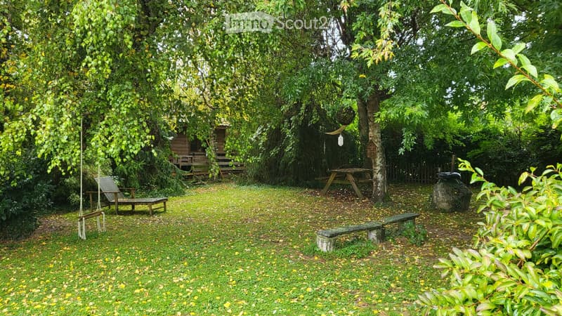 A lush garden with a swing, picnic table, wooden bench, and a small wooden cabin surrounded by trees and greenery.