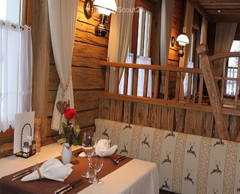 Cozy dining area with wooden furniture, set table with wine glasses, napkins, and a vase with flowers. Wooden walls and a staircase leading to an upper level.