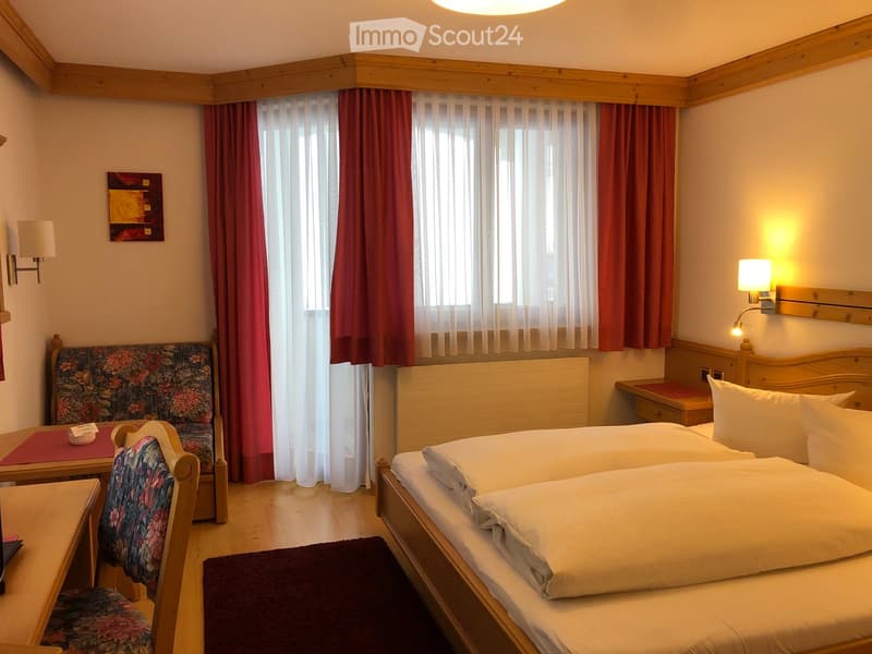 Cozy bedroom with two single beds, a small sofa, a wooden chair, a table, and a window with curtains.