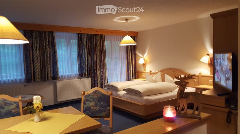 Cozy bedroom with a double bed, wooden furniture, a television, and decorative items including a candle and a small wooden moose figurine.