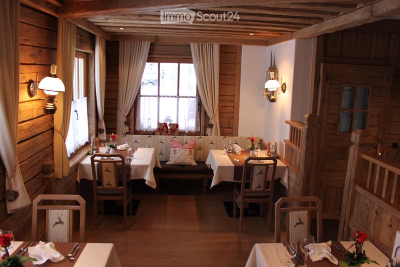 Cozy wooden-paneled dining area with tables, chairs, and a bench seating area, decorated with floral arrangements and warm lighting.