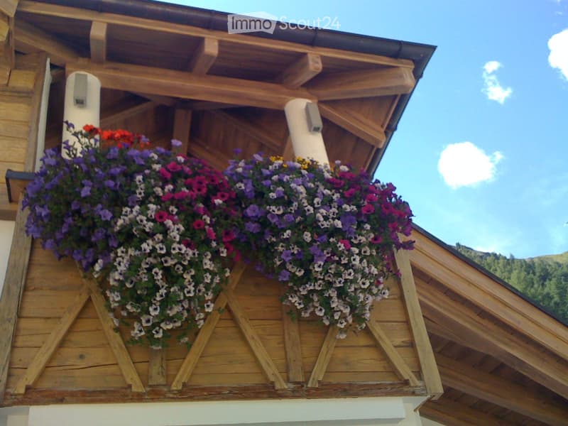Wooden balcony with colorful flower boxes, wooden beams, and a clear blue sky in the background.