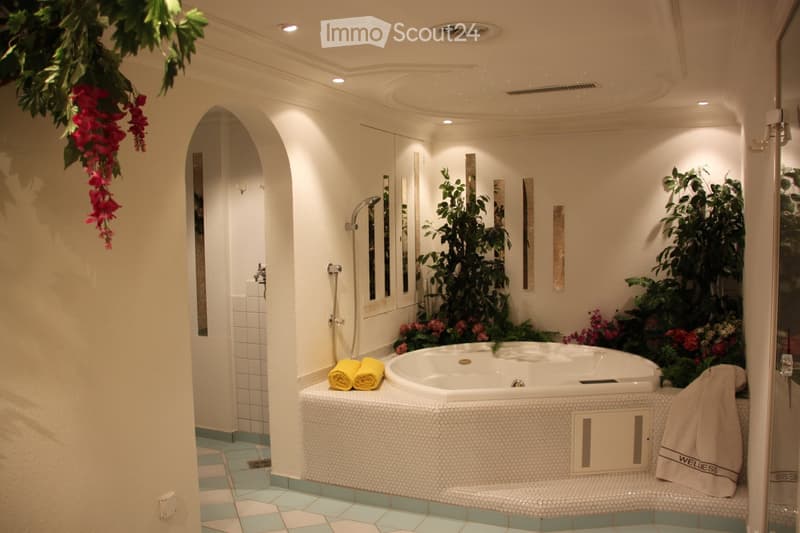 Luxurious bathroom with a large bathtub surrounded by plants and flowers, a shower area, and decorative mirrors.