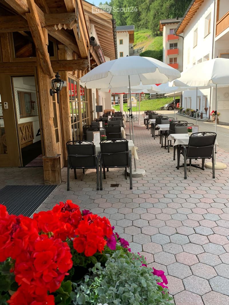 Outdoor seating area with tables, chairs, and umbrellas, surrounded by flowers and greenery.