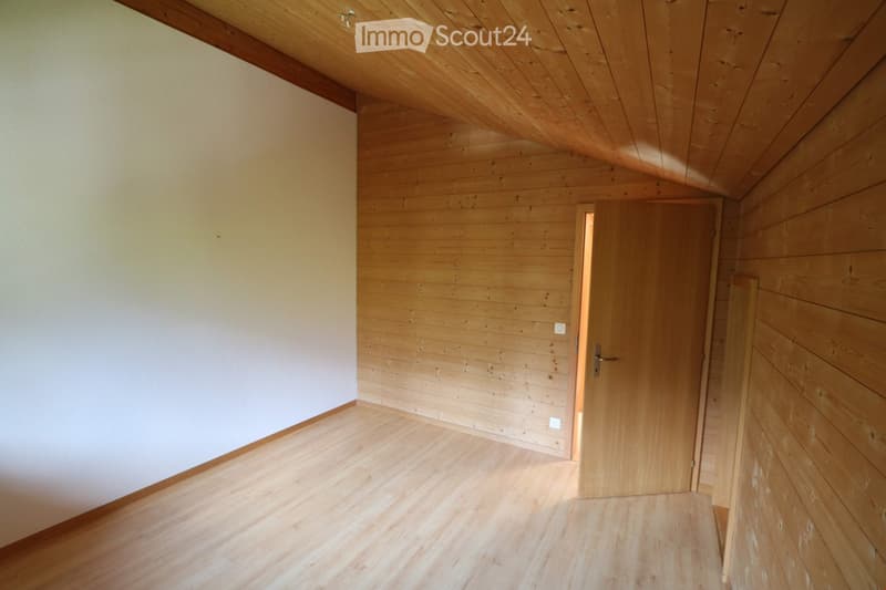 Empty room with wooden walls, wooden floor, and a wooden door leading to another space.