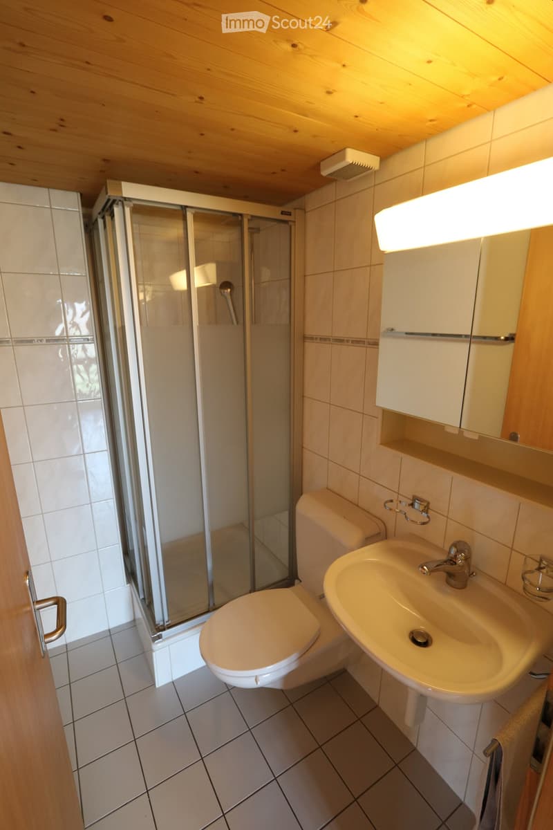 Modern bathroom with white tiled walls, a toilet, a sink with a faucet, a glass-enclosed shower, and a mirror above the sink.