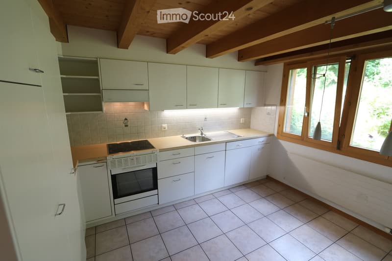 Bright kitchen with white cabinets, a central island, and a built-in oven and stove. The space features a tiled floor and large windows with wooden frames, allowing natural light to fill the room.