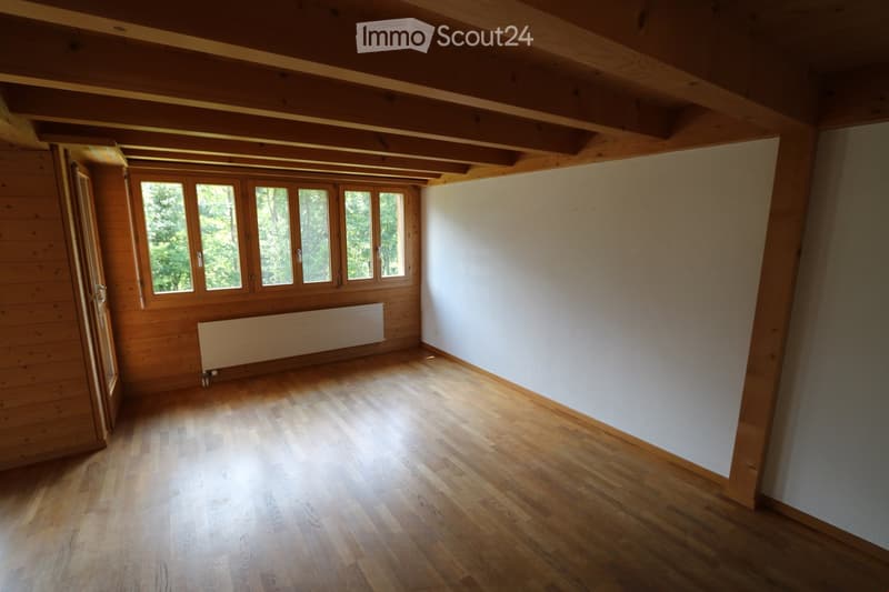 Empty room with wooden flooring, white walls, large windows, and exposed wooden beams on the ceiling.