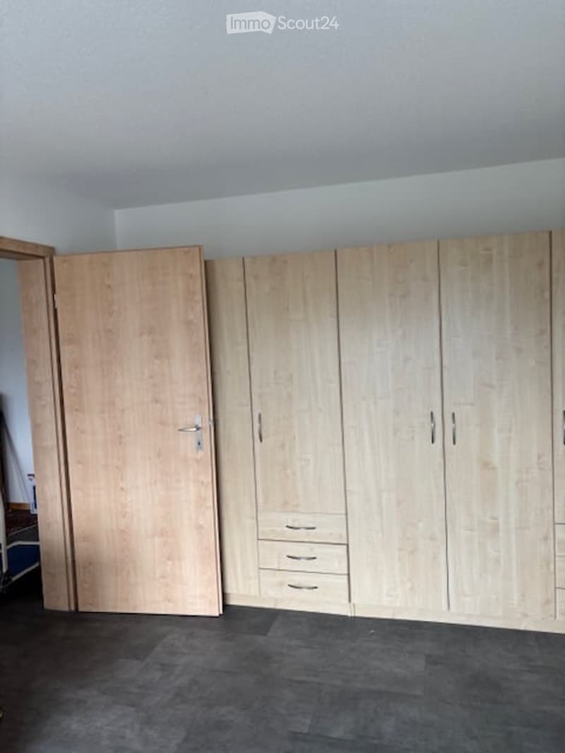 Empty room with light wooden built-in wardrobes and a dark grey carpeted floor.