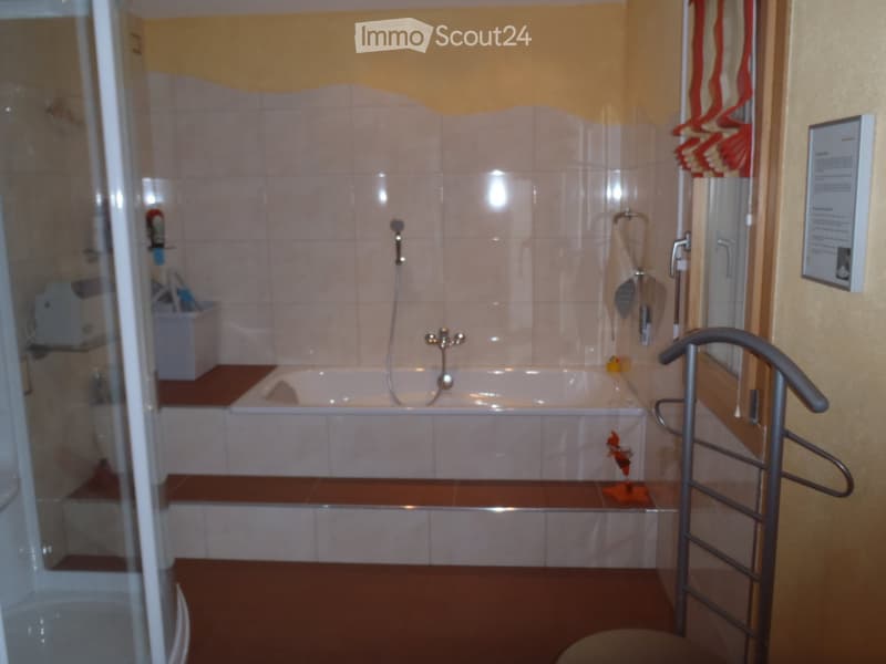Bathroom with a bathtub, tiled walls, a showerhead, a towel, and a toy in the tub.