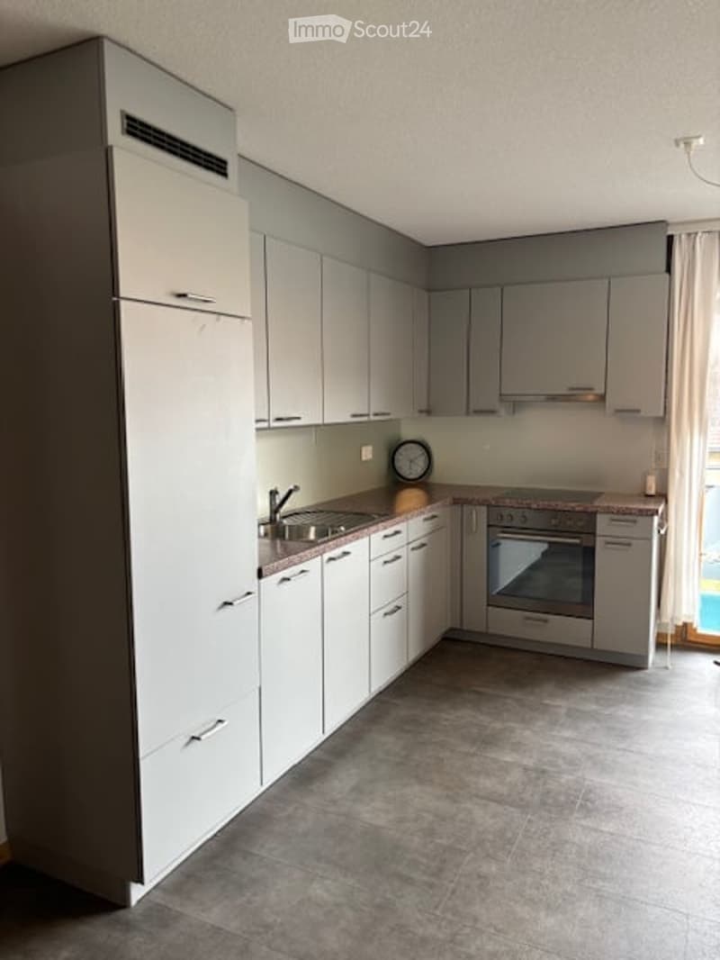 Modern kitchen with white and grey cabinets, stainless steel sink, oven, and a clock on the counter.