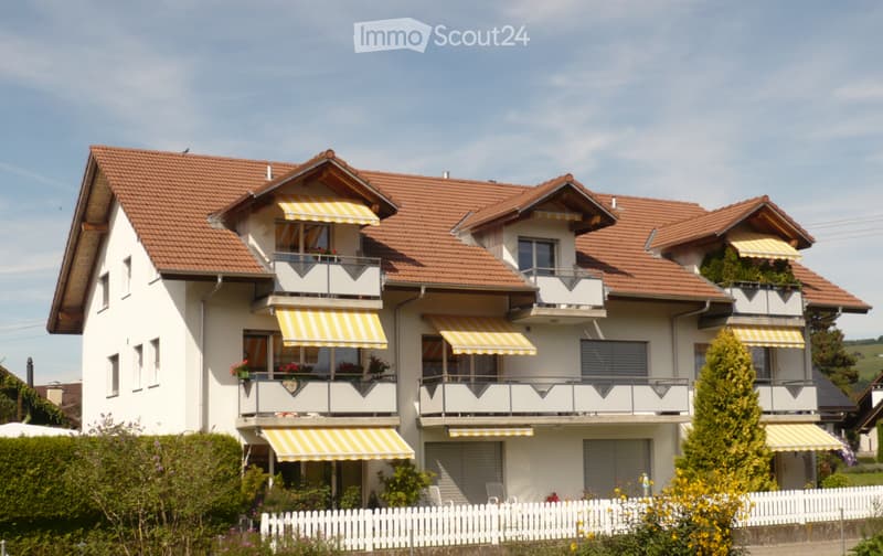 Two-story house with red-tiled roof, white exterior, multiple balconies with striped awnings, and a white picket fence in front.