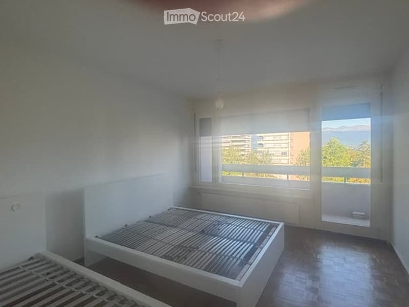 Minimalist bedroom with a single bed, large windows offering a view, and wooden flooring.
