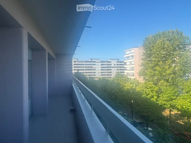 Modern balcony with a clean, minimalist design, overlooking a cityscape with buildings and greenery.