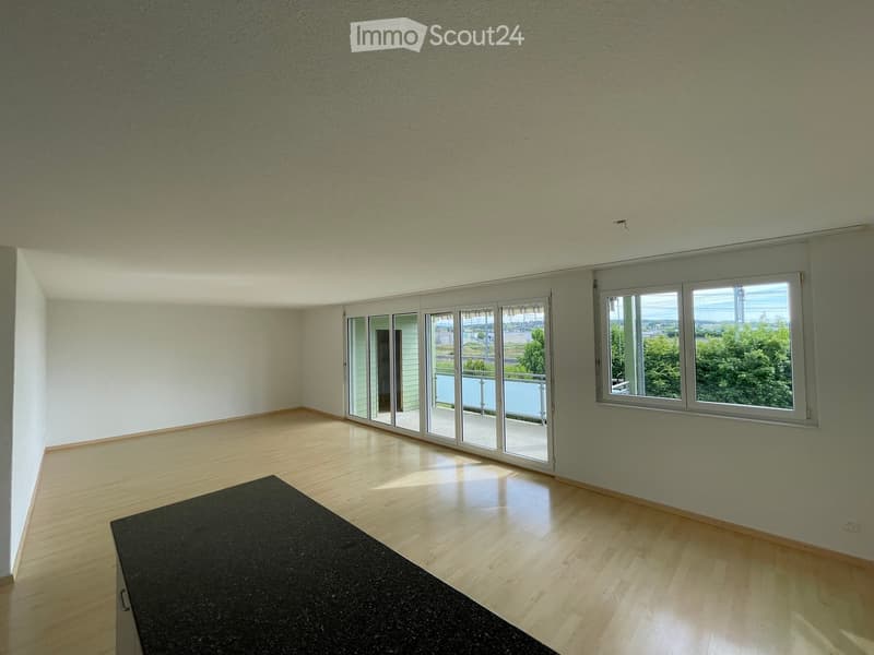 Empty room with light green walls, wooden flooring, large windows, and sliding glass doors leading to a balcony.