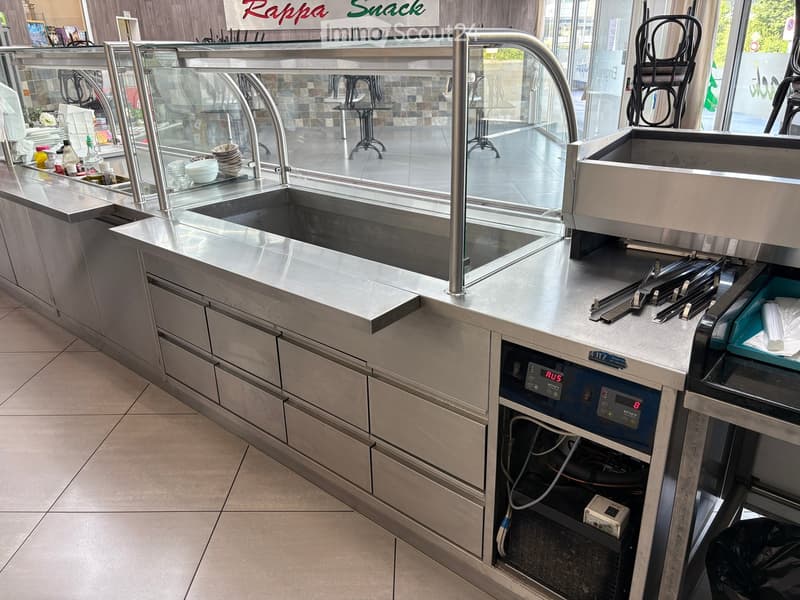 Modern commercial kitchen with stainless steel counters, sink, and appliances.