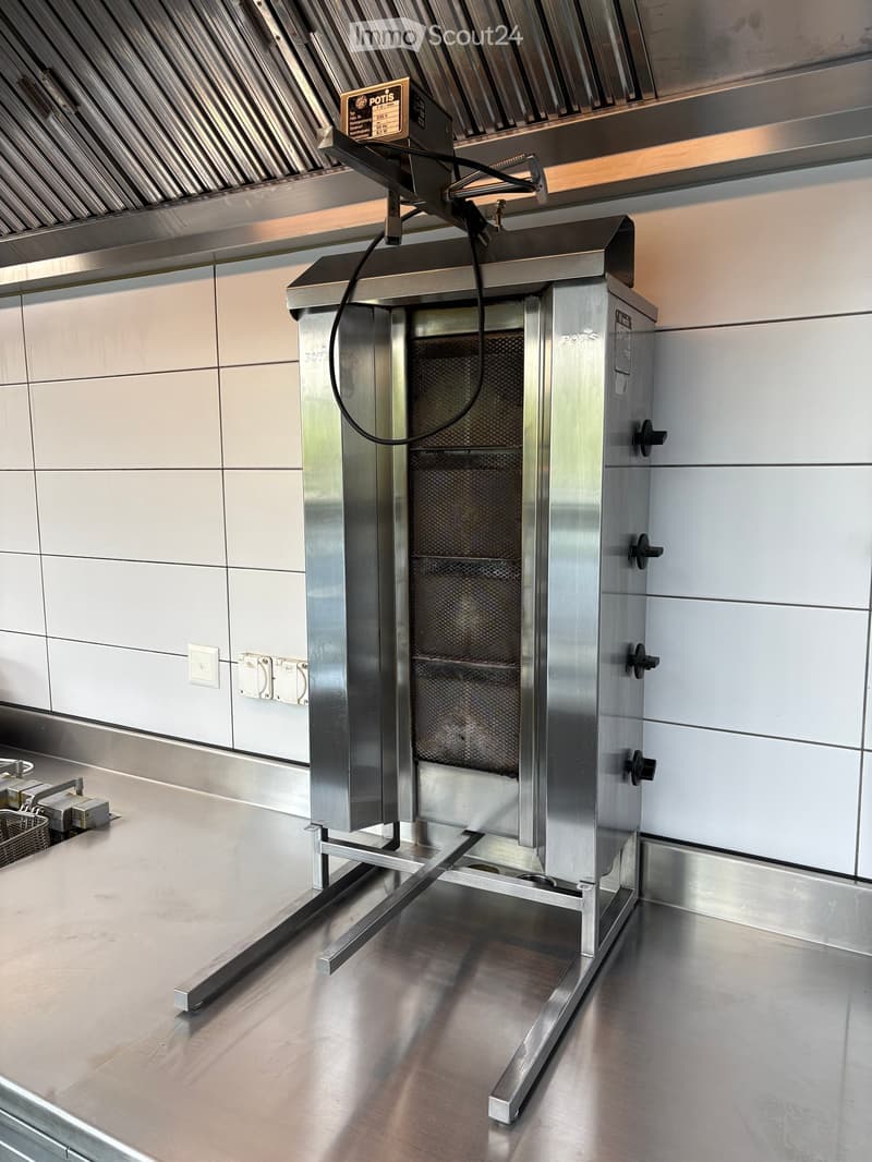 Stainless steel commercial kitchen with a large oven and a range hood above it, featuring sleek, modern design with stainless steel surfaces and tiled walls.