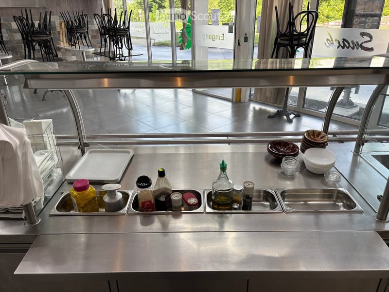 Stainless steel kitchen sink area with multiple compartments, various bottles and containers, and a tray on the counter.