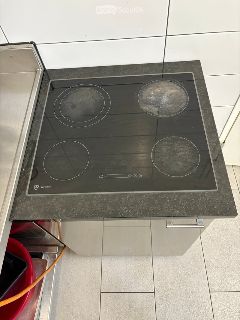 Induction cooktop with four circular cooking zones, placed on a dark countertop with a stainless steel backsplash.