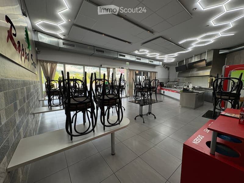 Restaurant interior with tiled floor, modern lighting, several tables and chairs, kitchen area with appliances and counters.